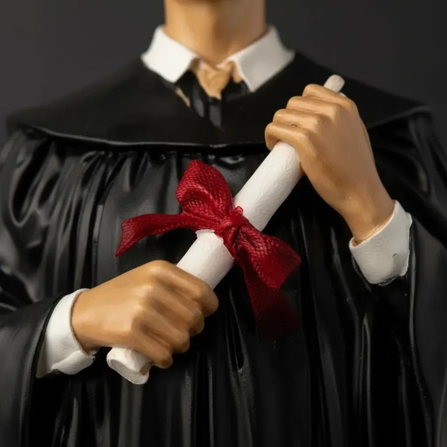 Detalle de las manos de la figura sosteniendo el diploma con cinta roja